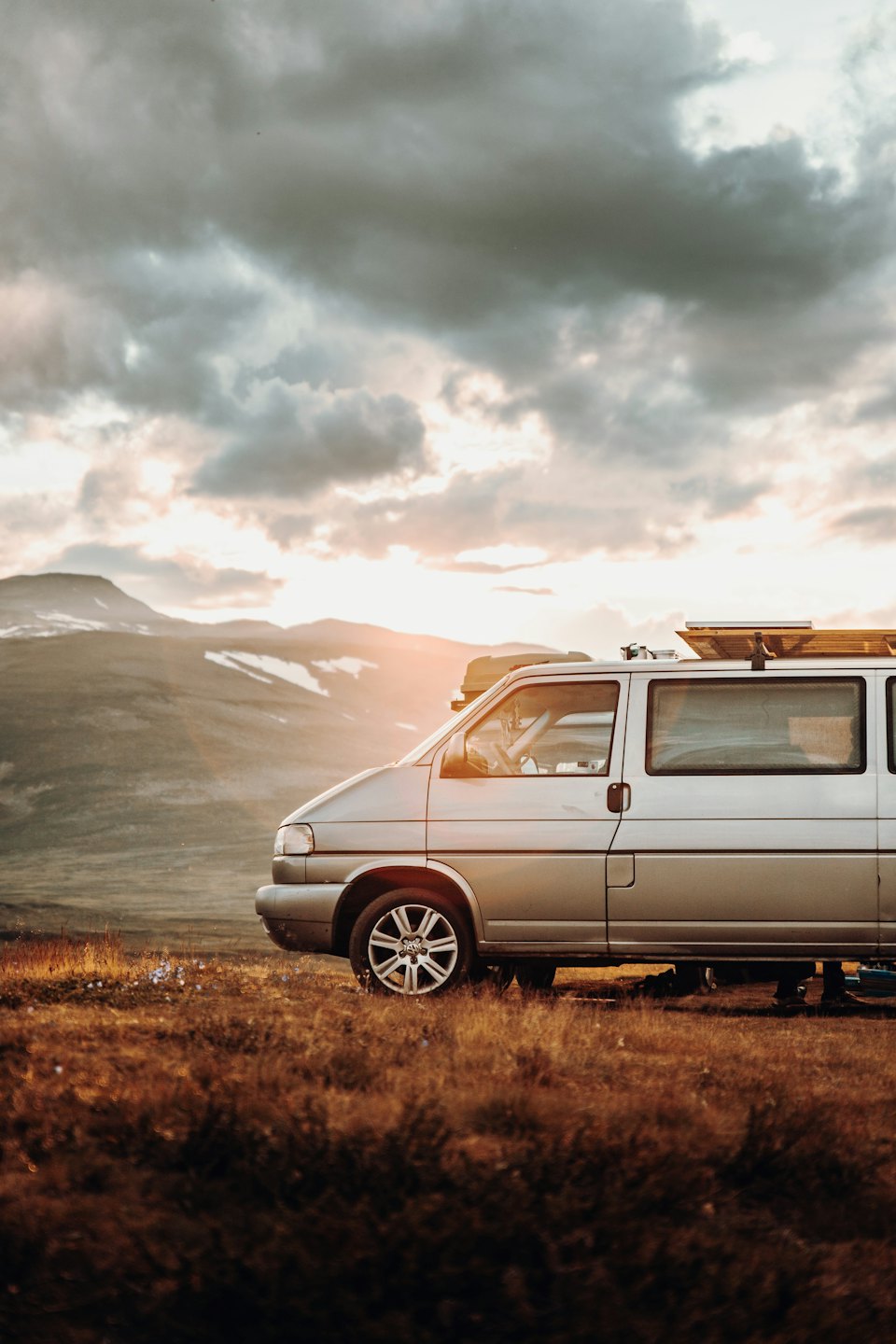 Ein silberner Campervan, der auf einem grasbewachsenen Berghang parkt.