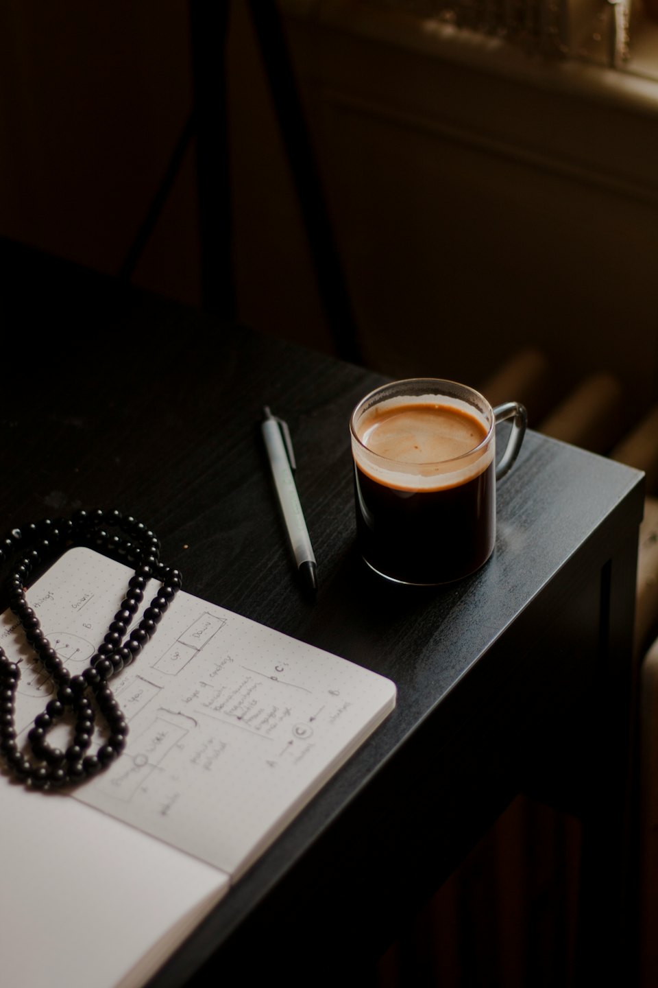 Ein schwarzer Schreibtisch mit einem offenen Notizbuch, Kaffee und Stift.