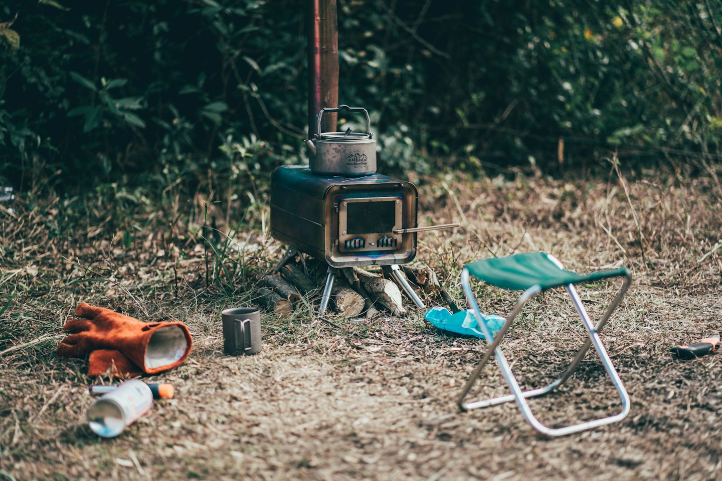 Ein Campingkocher und ein Wasserkocher stehen auf Gras neben Outdoor-Ausrüstung.
