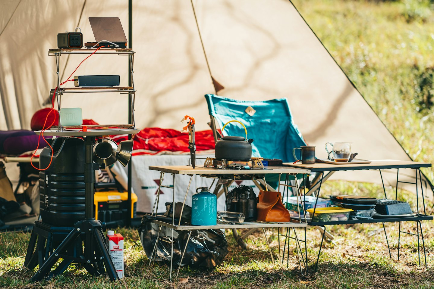Organisierte Campingausrüstung auf Regalen und Tischen vor einem Zelt.