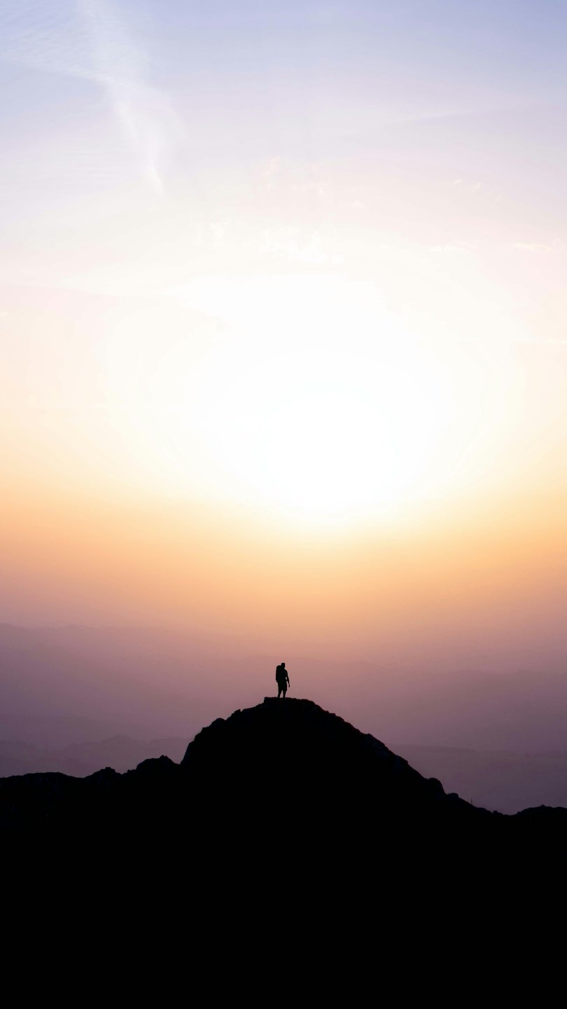 Silhouette eines Rucksacktouristen auf einem Berggipfel bei Sonnenaufgang.