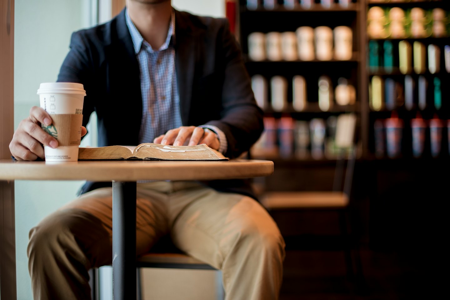 Mann liest ein Buch am Cafétisch mit Kaffee.