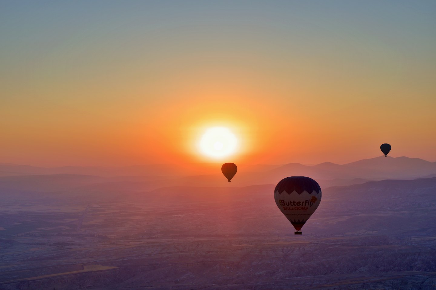 Heißluftballons schweben bei Sonnenaufgang über einer weiten Berglandschaft.