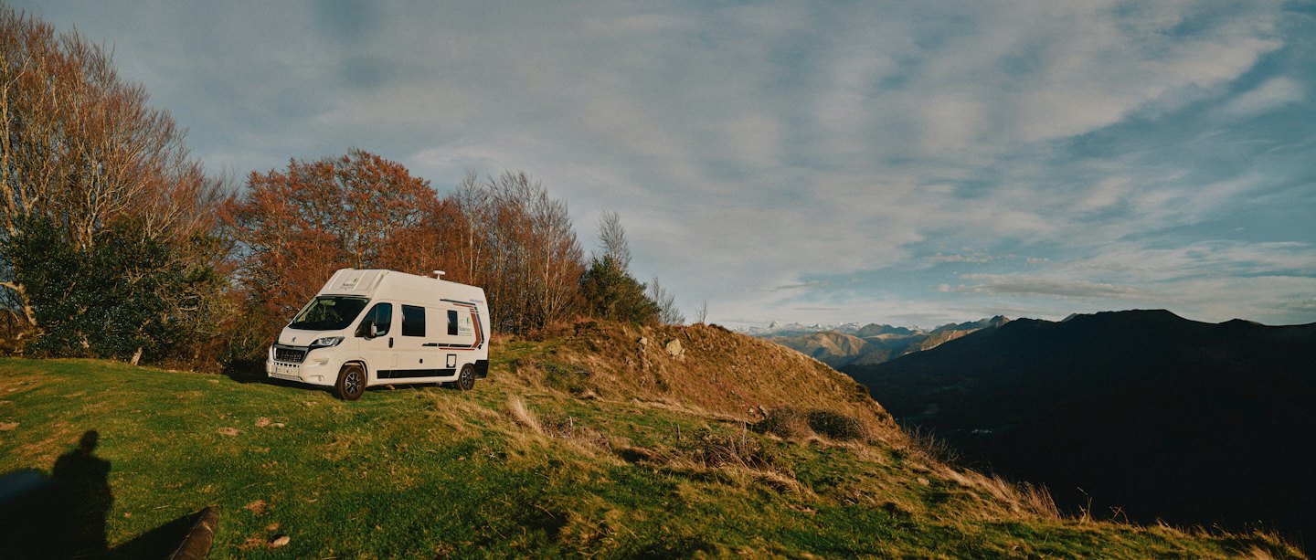 Ein weißer Campervan, der auf einem grasbewachsenen Berghang parkt.